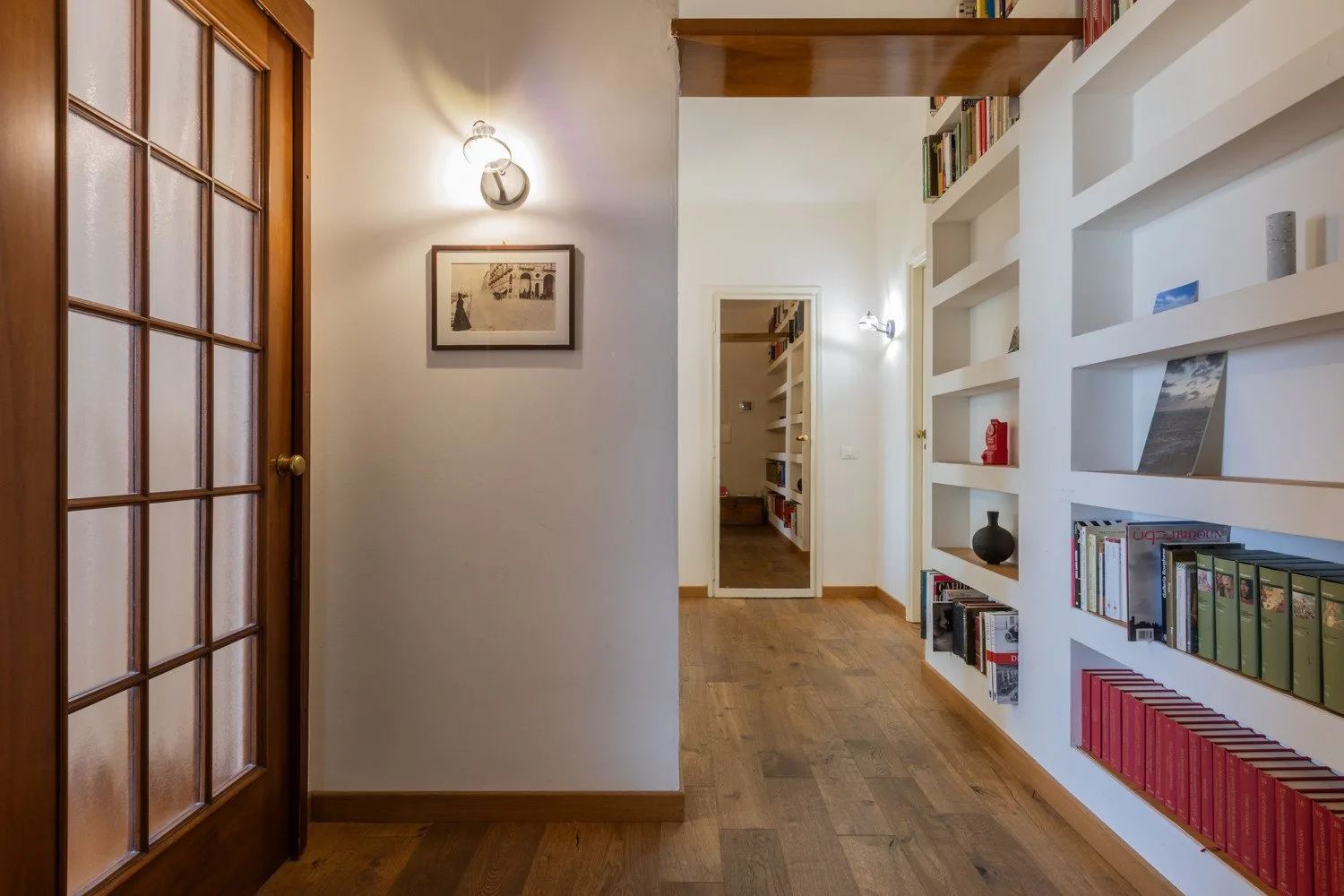 Un pasillo con estanterías empotradas con libros y suelo de madera.