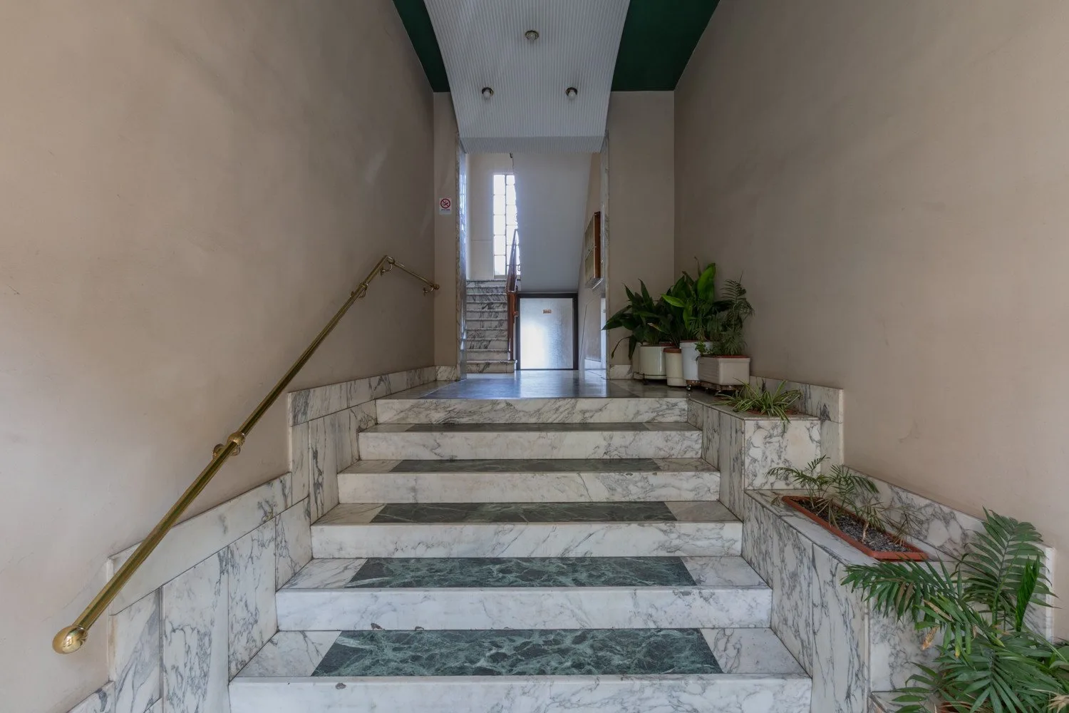Una escalera de mármol conduce a un pasillo interior iluminado con plantas en macetas.