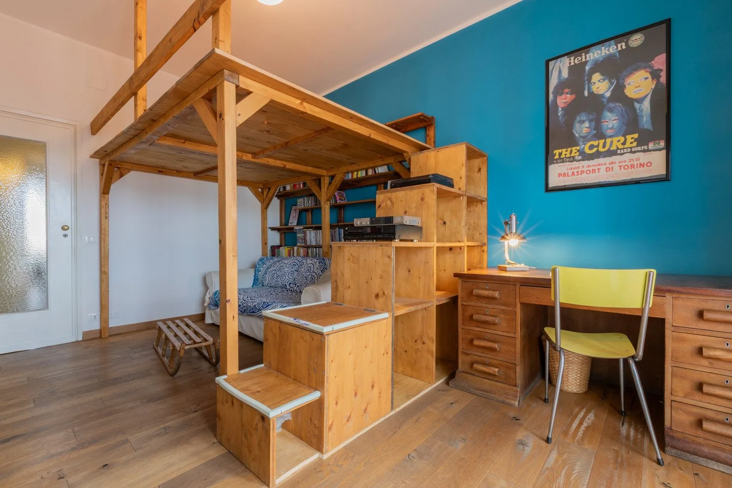 Una cama alta de madera y un escritorio amueblan un dormitorio colorido.