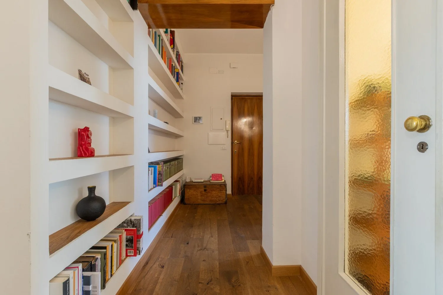 Un pasillo estrecho con estanterías empotradas y suelo de madera.
