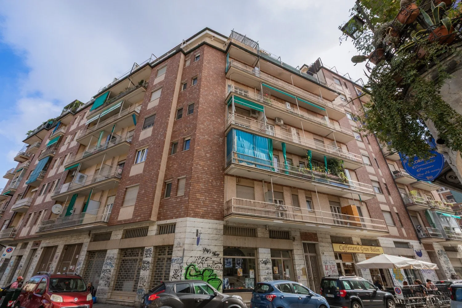 Un edificio de apartamentos de varios pisos da a una calle urbana, con balcones y comercios a nivel de calle.