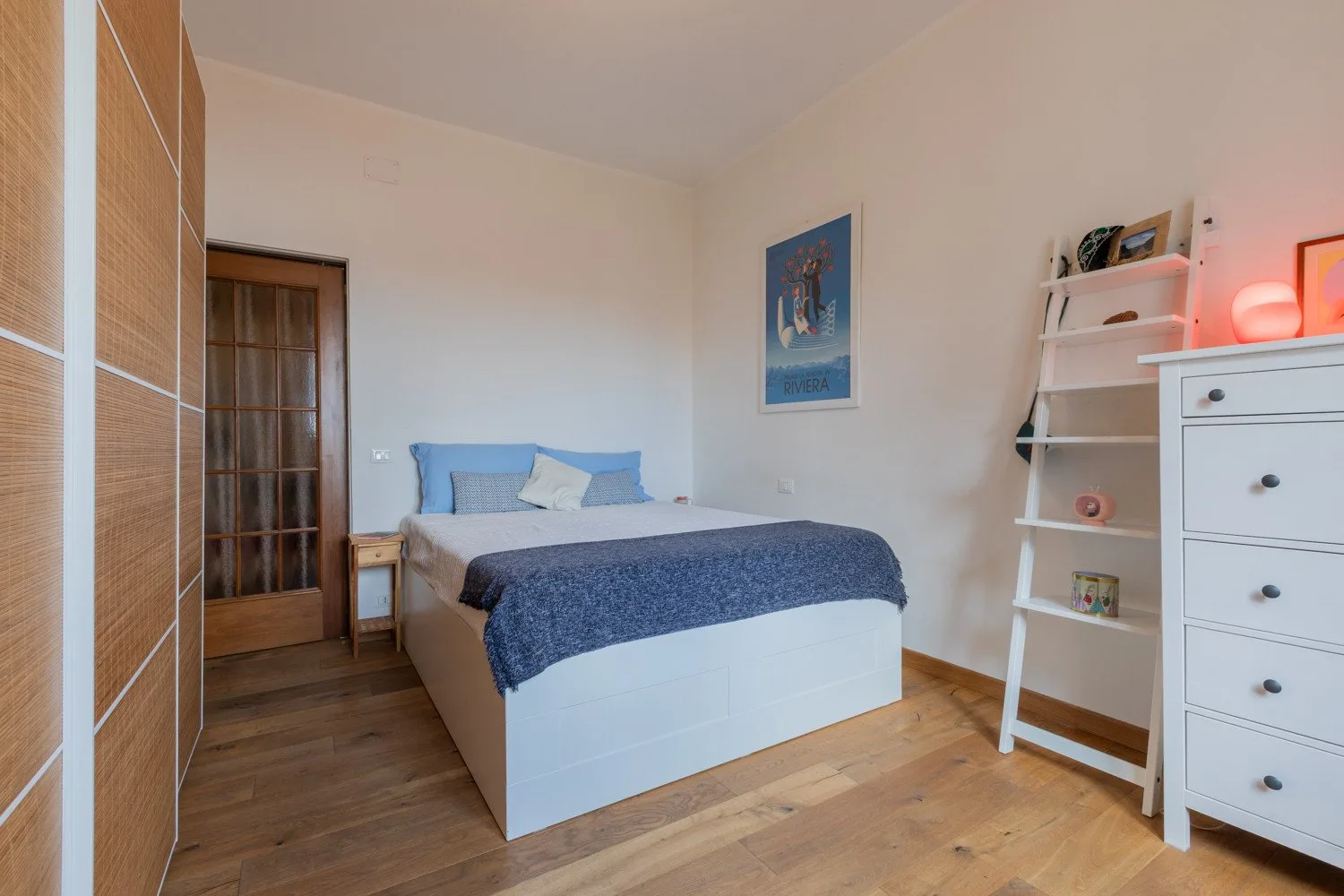 Un dormitorio con una cama, una puerta de madera y paredes claras.