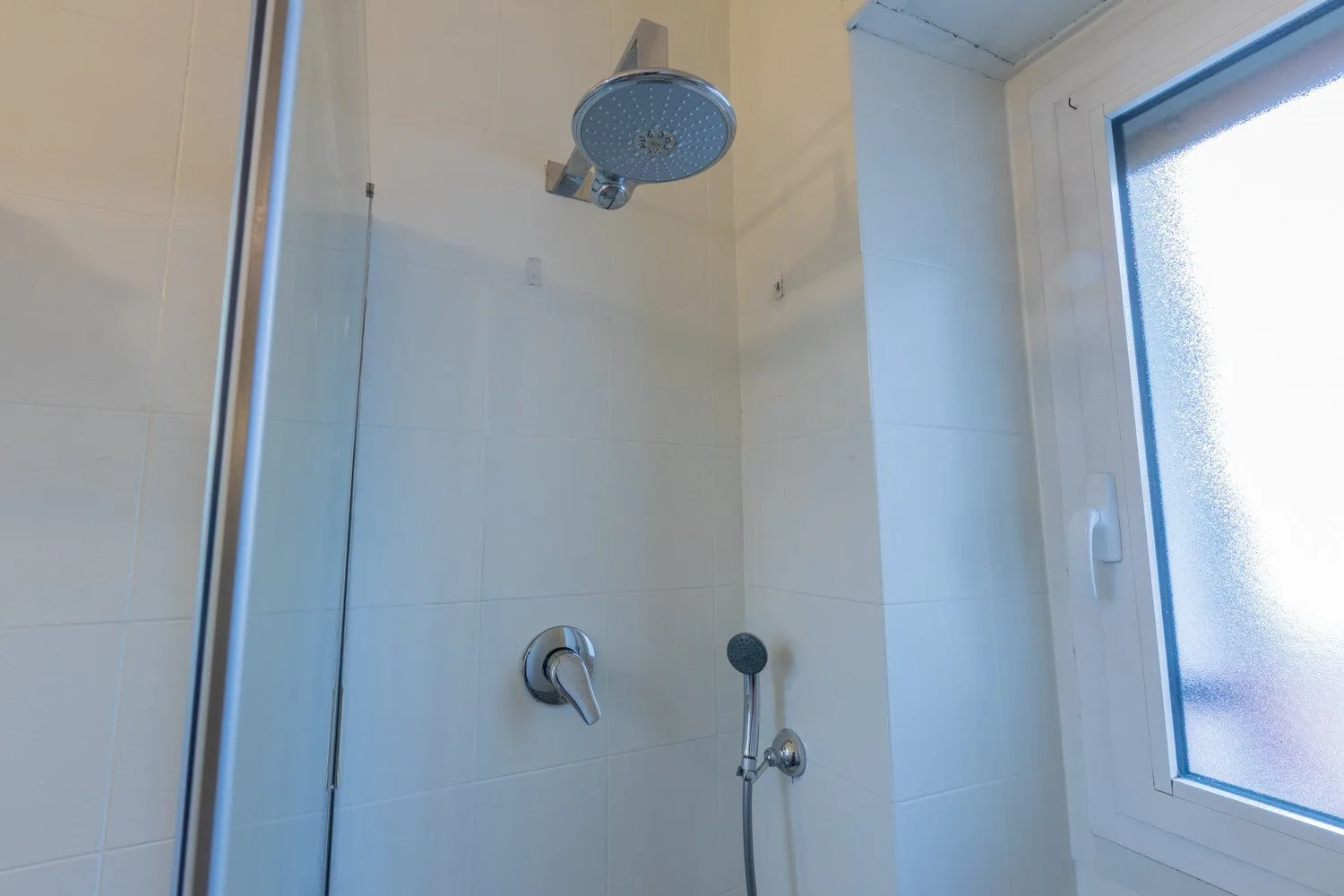 Una zona de ducha con azulejos junto a una ventana translúcida.