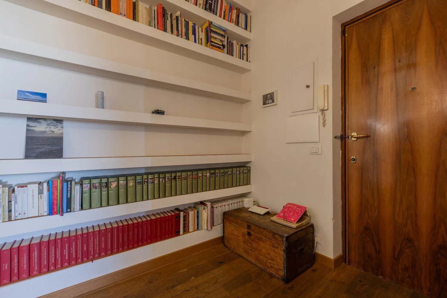 Una habitación con largas estanterías de libros junto a una puerta de madera.