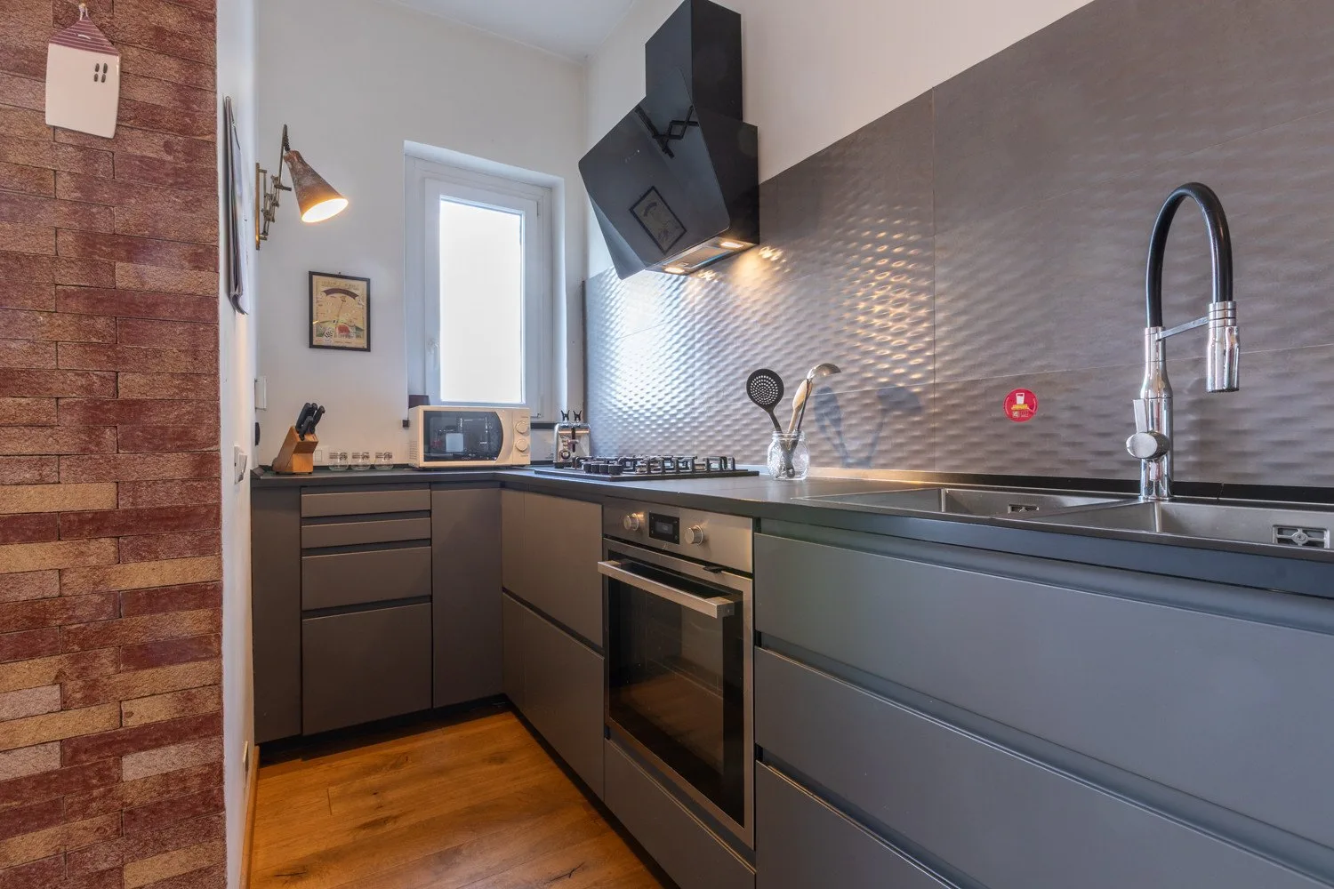 Una cocina moderna con gabinetes oscuros, una placa de cocina y un fregadero de acero inoxidable.