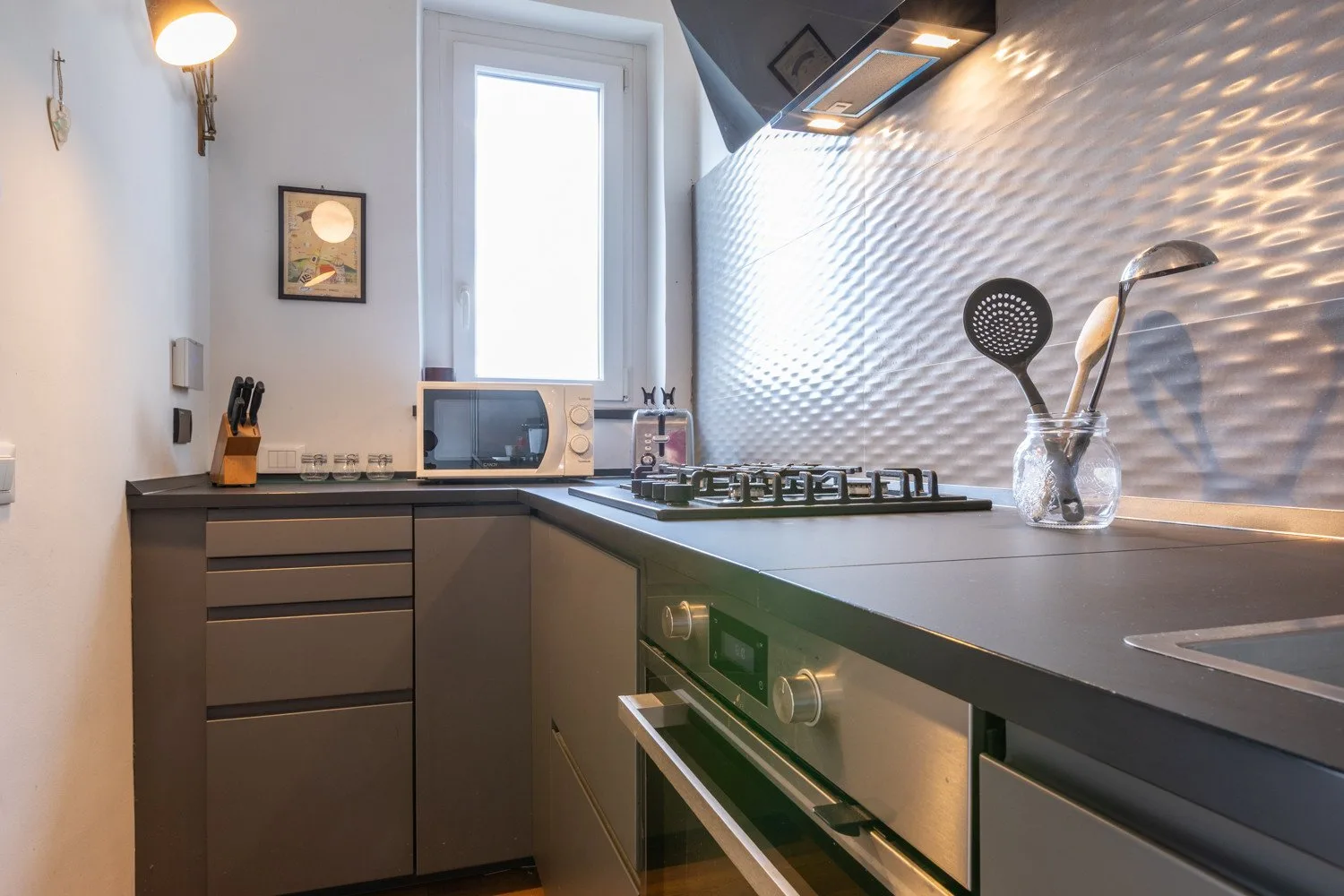Una cocina moderna con encimeras oscuras, una placa de cocina y una ventana sobre la encimera.