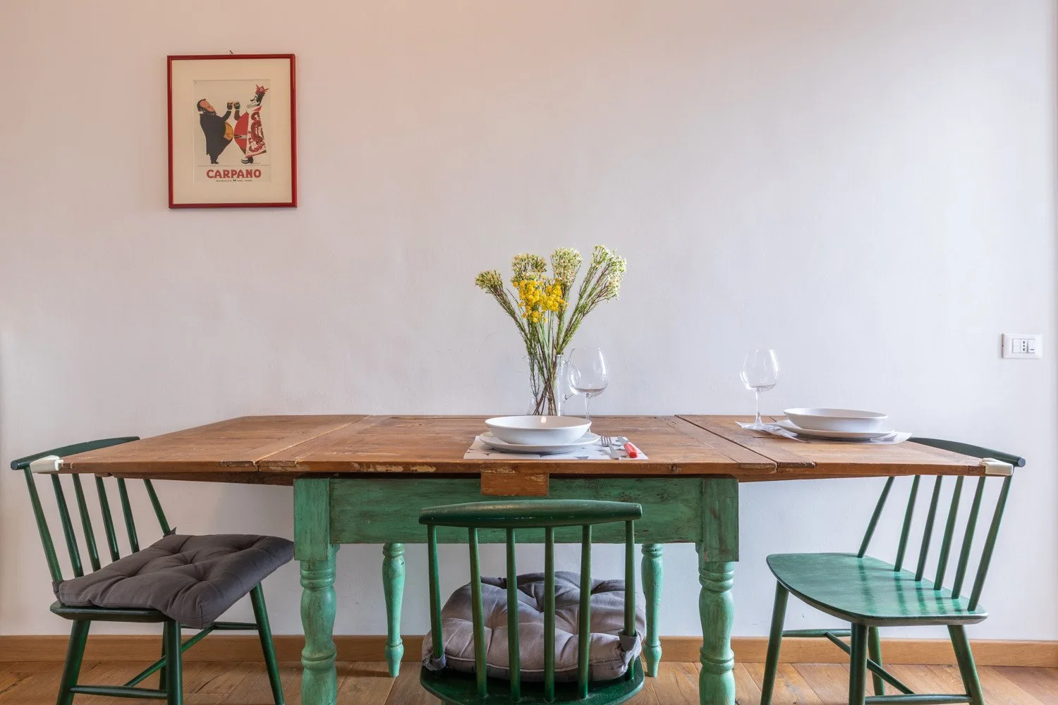 Comedor con una mesa de madera, platos, copas y flores.
