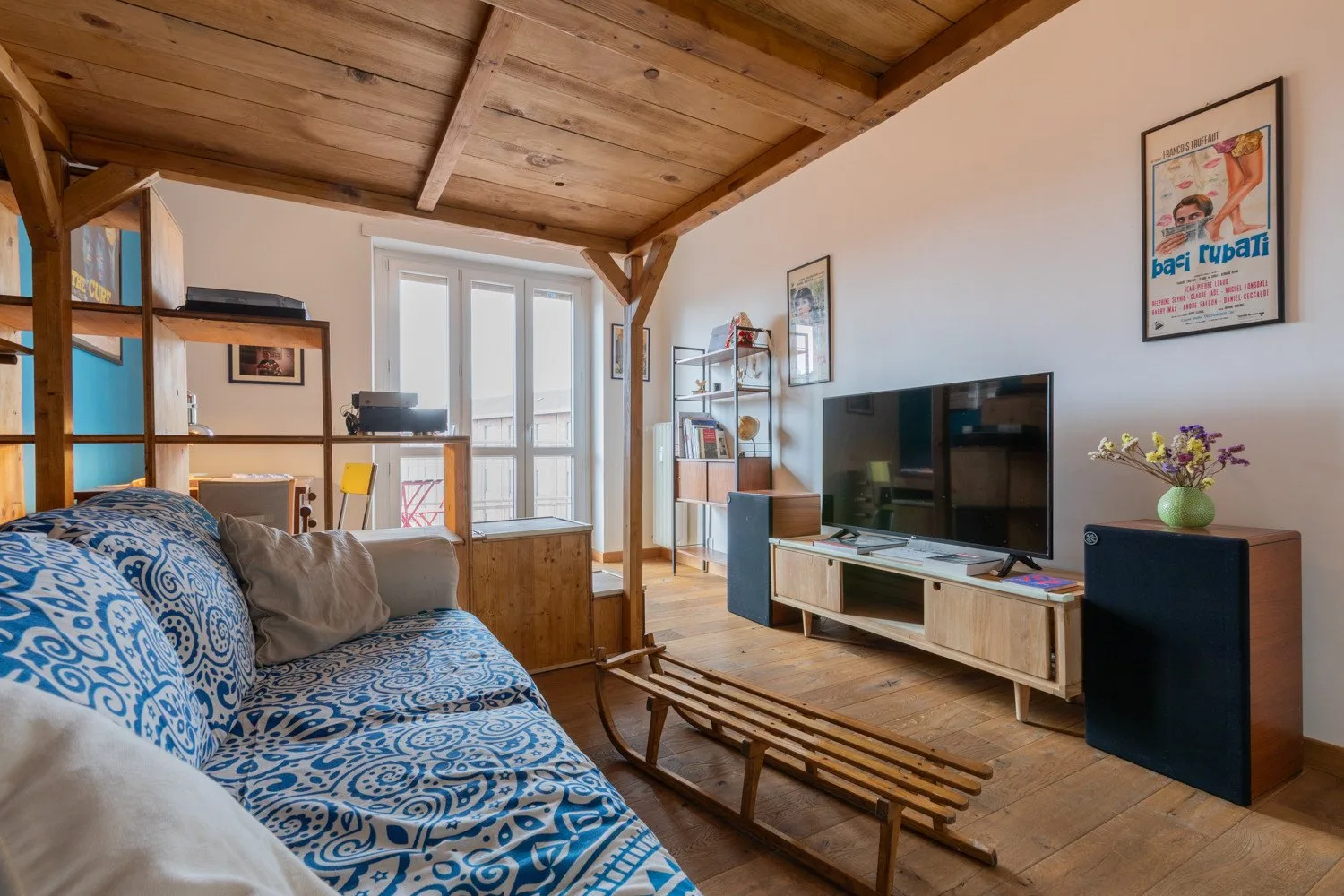 Una sala de estar con asientos estampados, un televisor y techo de madera.