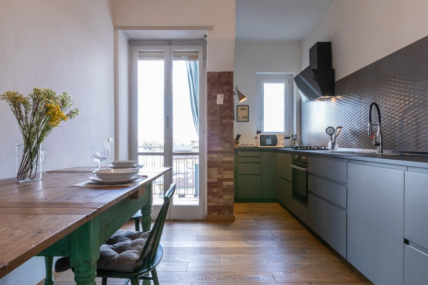 Cocina y comedor con gabinetes verdes y una mesa de madera.