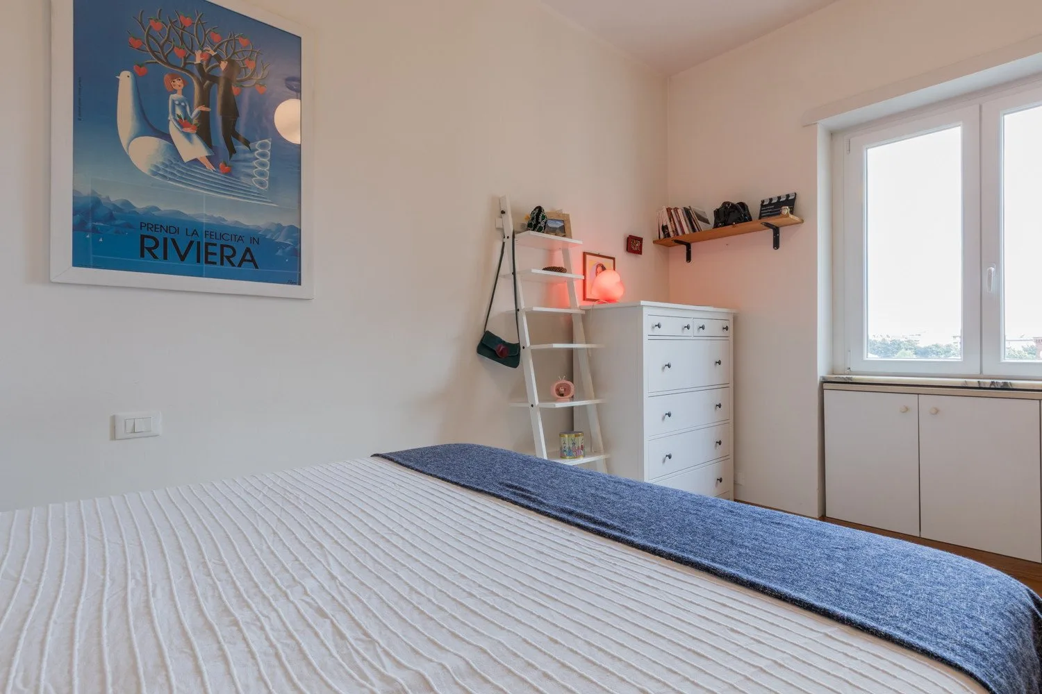 Un dormitorio con una cama, una cómoda blanca y una ventana grande.