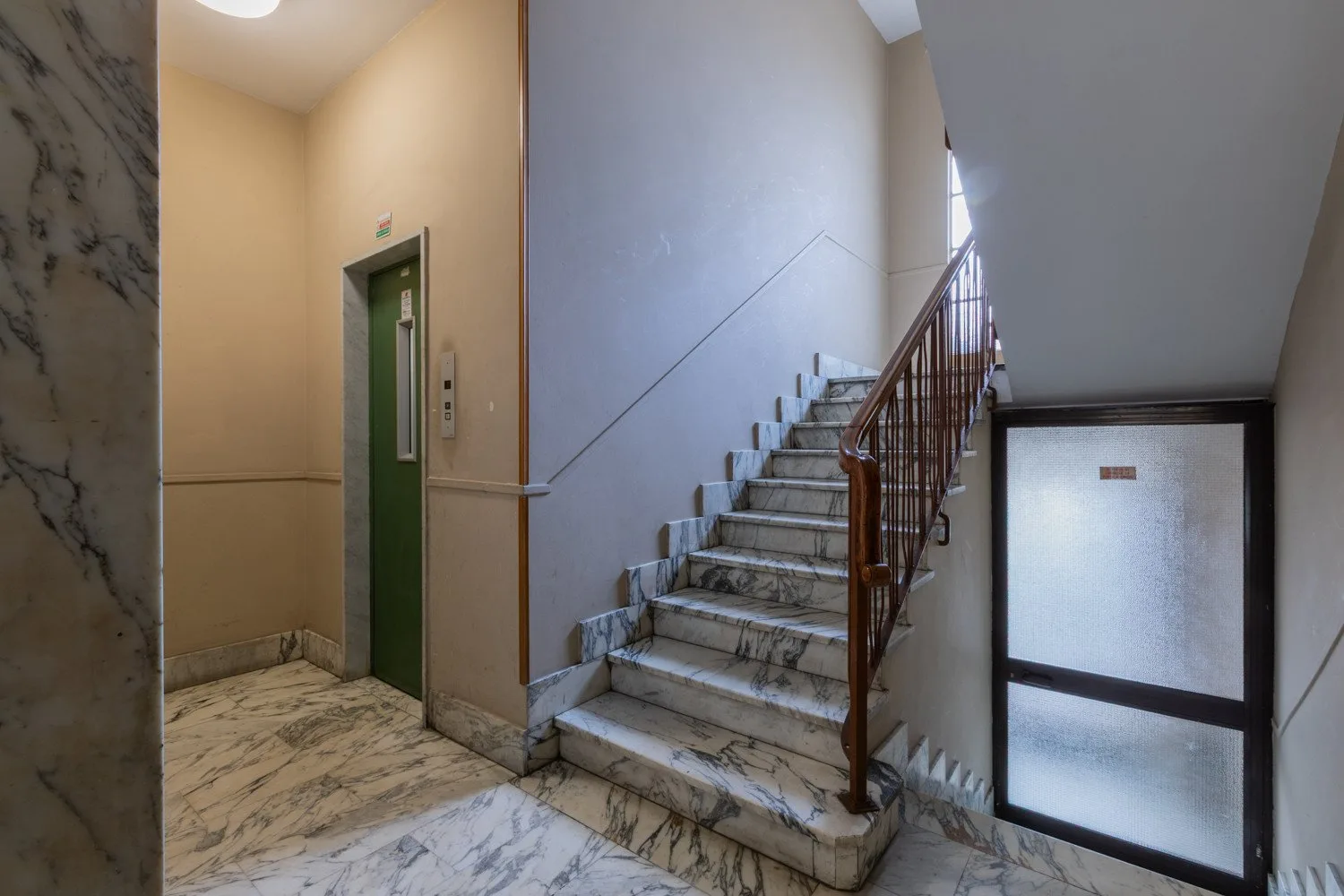 Un hueco de escalera con suelo de mármol, ascensor y escaleras.