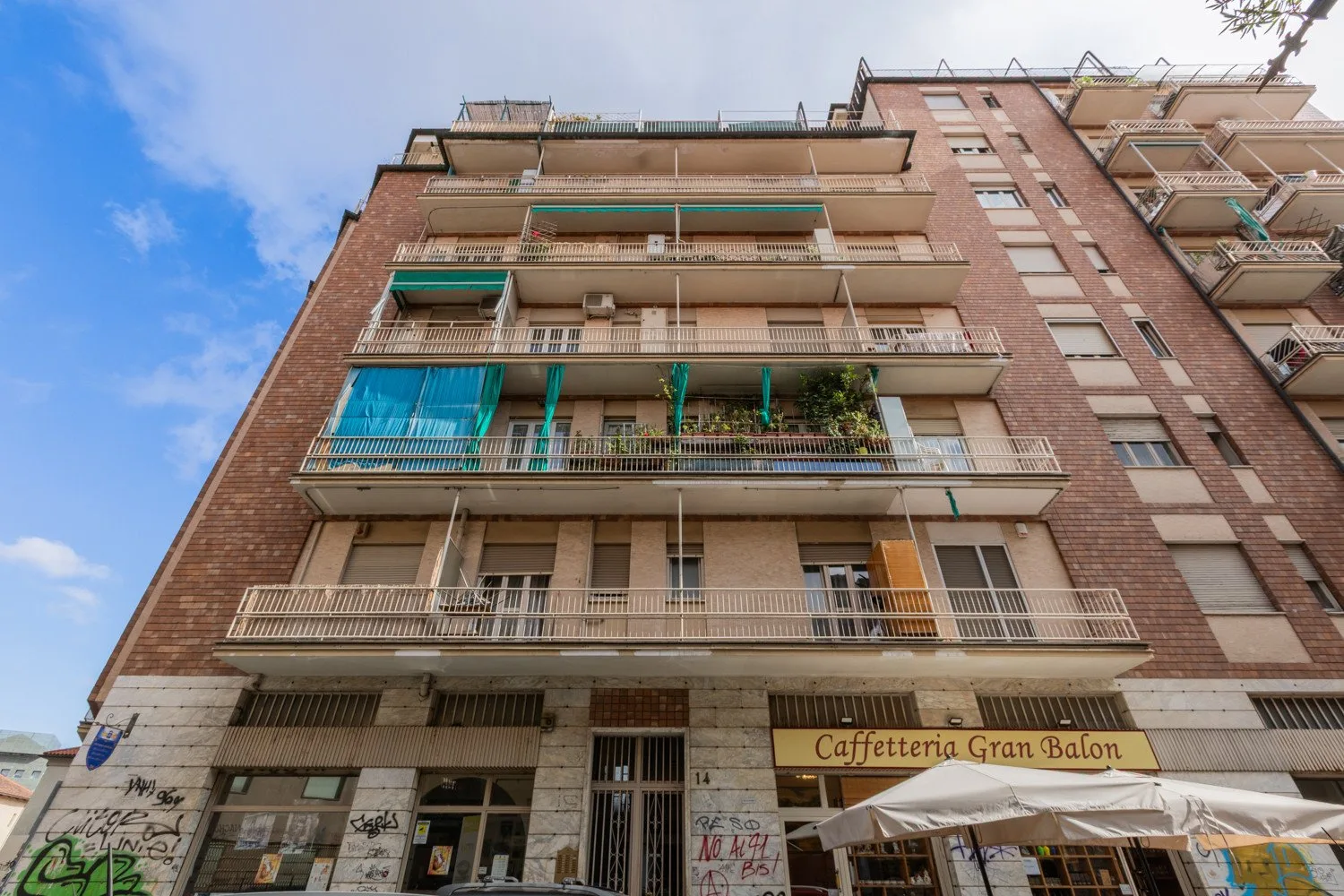 Un edificio de ladrillo de varios pisos con balcones se eleva sobre locales a pie de calle.