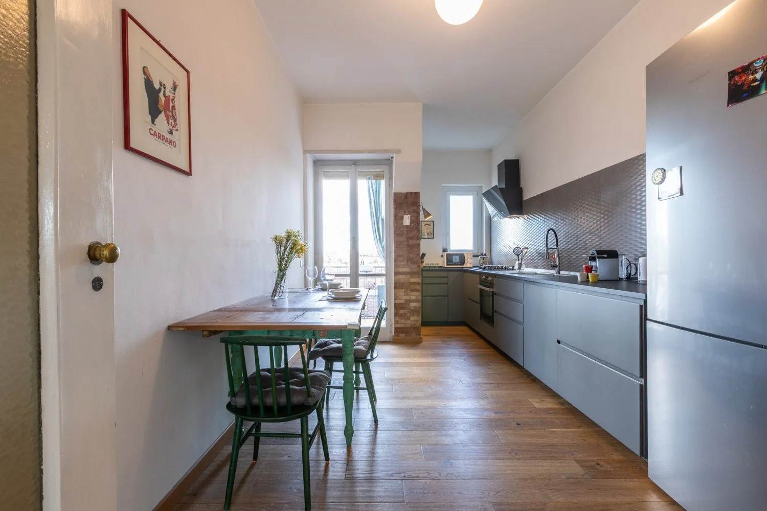 Una cocina estrecha con una mesa de comedor y sillas verdes junto a la encimera.