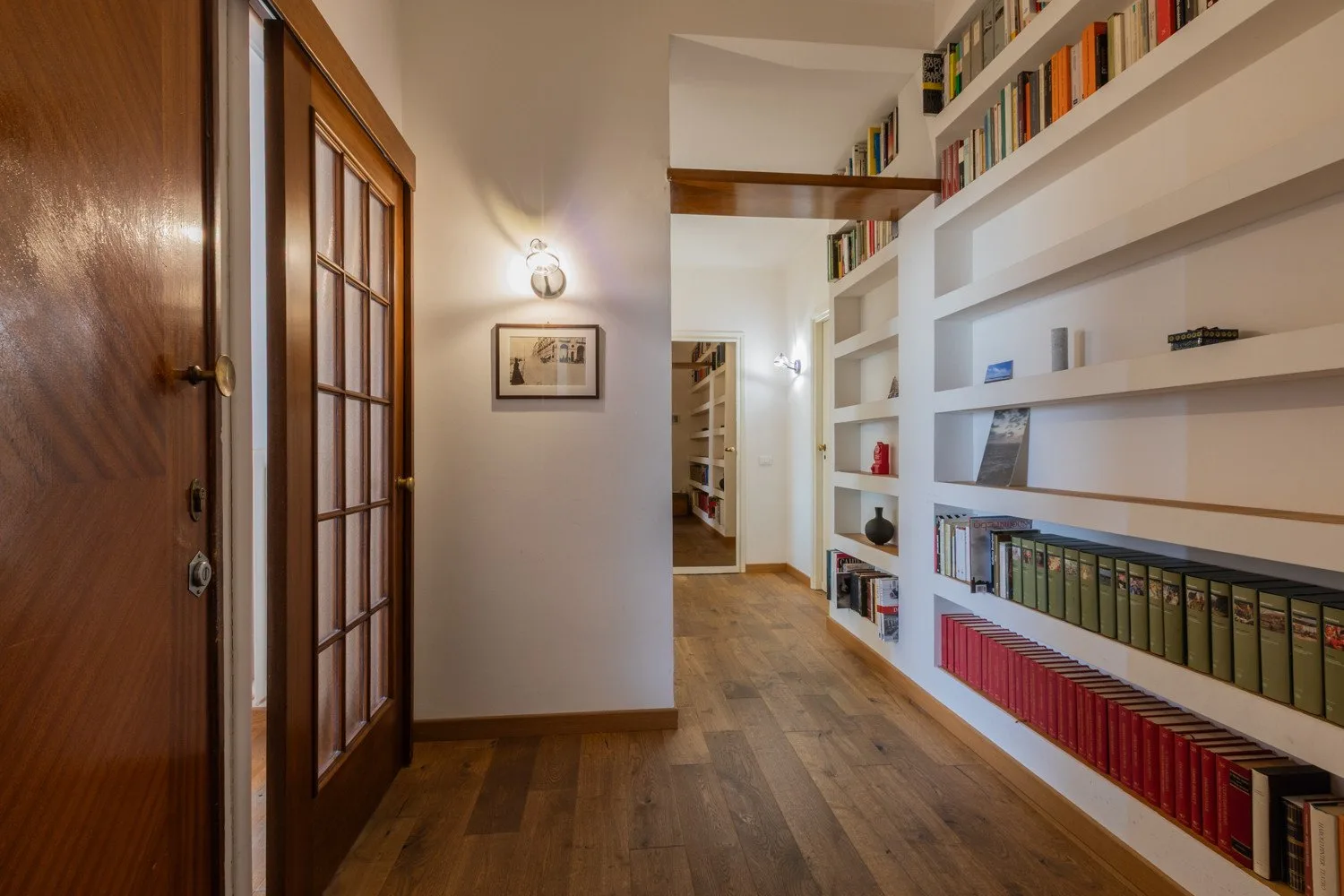 Un pasillo con suelo de madera y estanterías empotradas a lo largo de una pared.