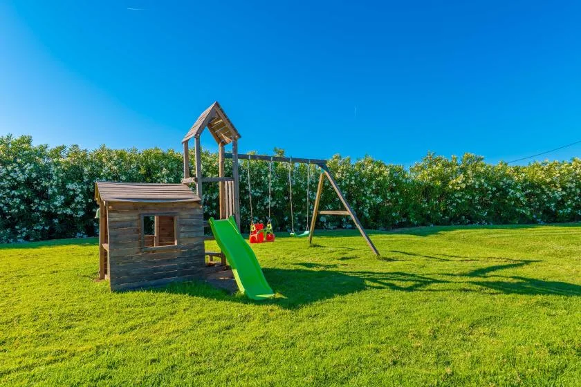 Zona de juegos en un patio con una estructura de madera, un tobogán y un columpio.