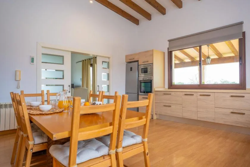 Comedor con una mesa de madera junto a una cocina y una ventana amplia.