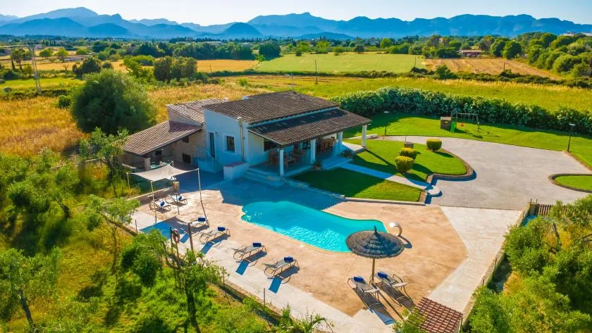 Una casa y una piscina están rodeadas de campos, con montañas a lo lejos.