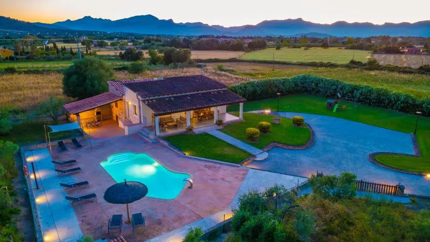 Una piscina al aire libre y un patio pavimentado junto a una casa, con campos y montañas al fondo.