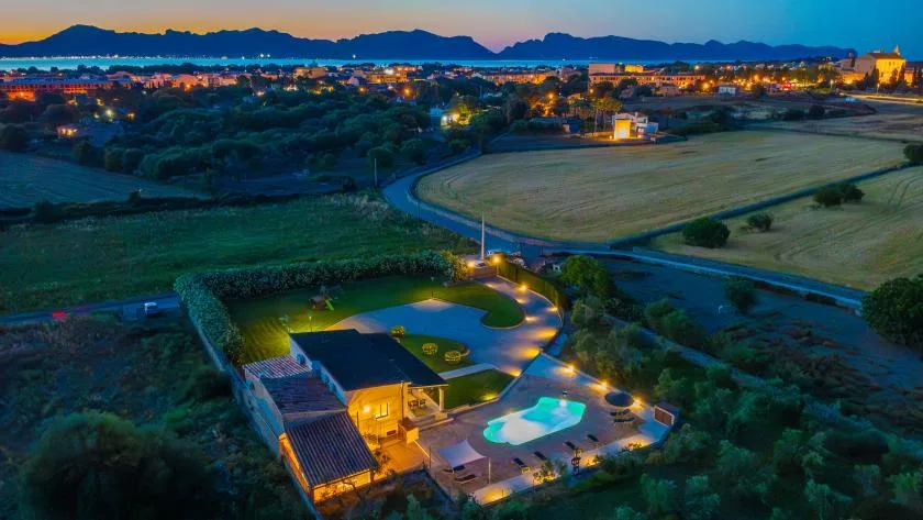 Una propiedad rural con una piscina iluminada y campos alrededor al anochecer.