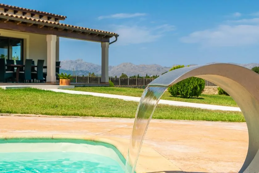 Una piscina junto a un patio cubierto, con una fuente de agua curva.