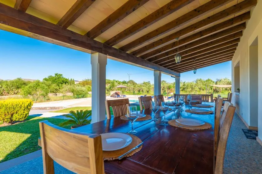 Un comedor exterior cubierto con una mesa larga de madera y sillas da a un jardín.