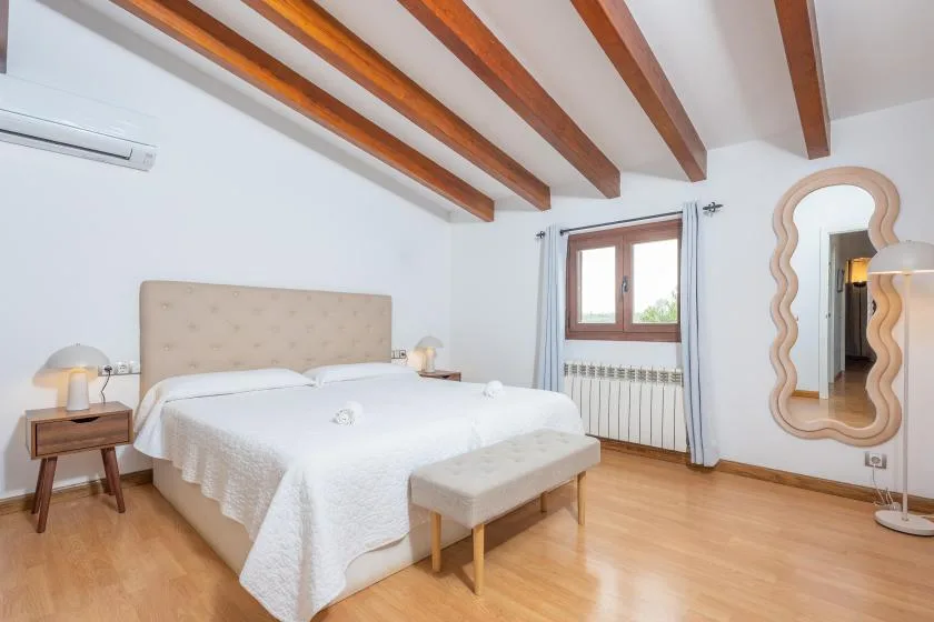 Un dormitorio luminoso con una cama grande y vigas de madera a la vista.