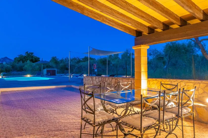 Una zona de comedor al aire libre cubierta, con asientos metálicos junto a una piscina.