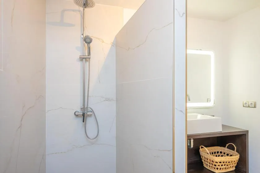 Un baño con una ducha de pared y un lavabo junto a un espejo iluminado.