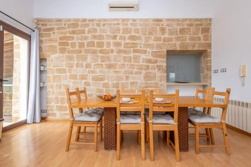 Comedor con una mesa de madera y asientos junto a una pared de piedra.