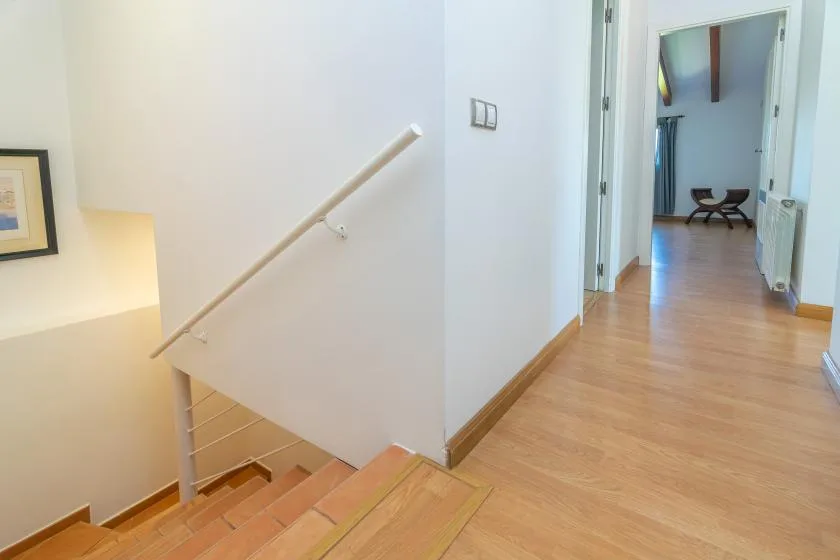 Un pasillo luminoso con suelo de madera y una escalera con pasamanos.