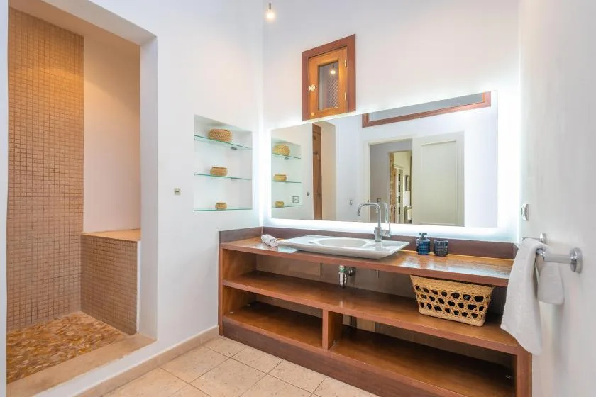 Un tocador de baño con lavabo, espejo y estantes abiertos de madera.