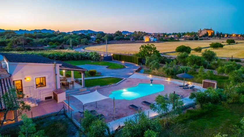 Una piscina al aire libre y un patio pavimentado junto a un edificio bajo, con campos al fondo.