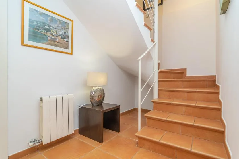 Una escalera de baldosas sube junto a una mesa pequeña y un radiador de pared.