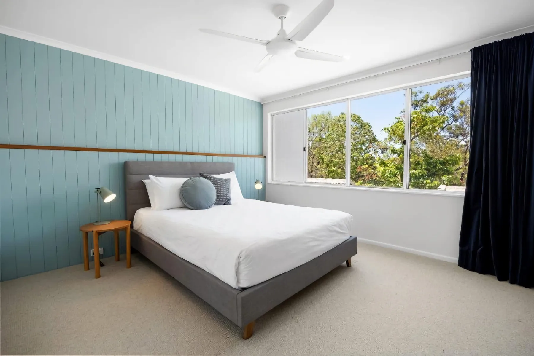 A bedroom with a bed beside a large window overlooking trees.