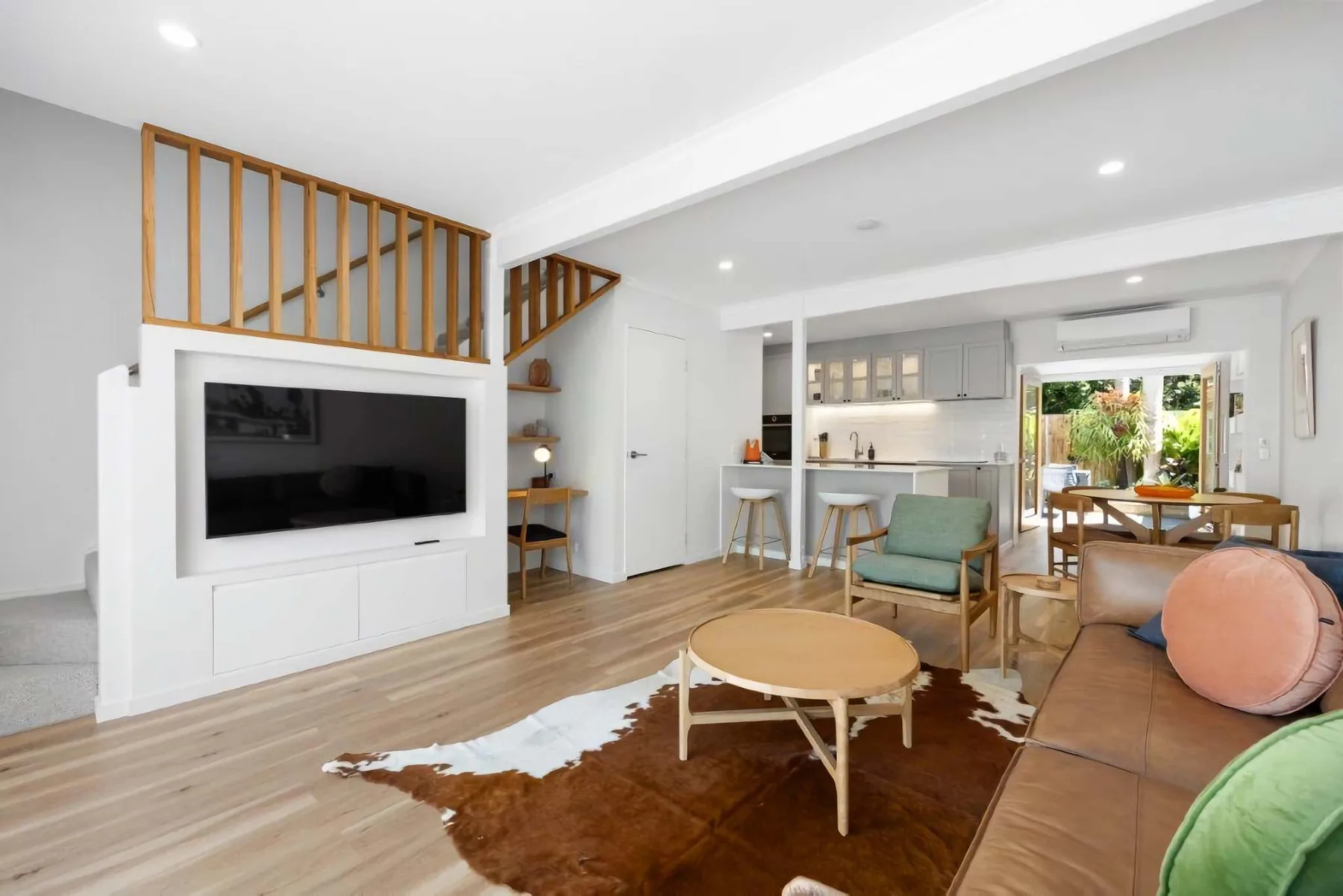 A bright living room with a television, seating, and an open kitchen.