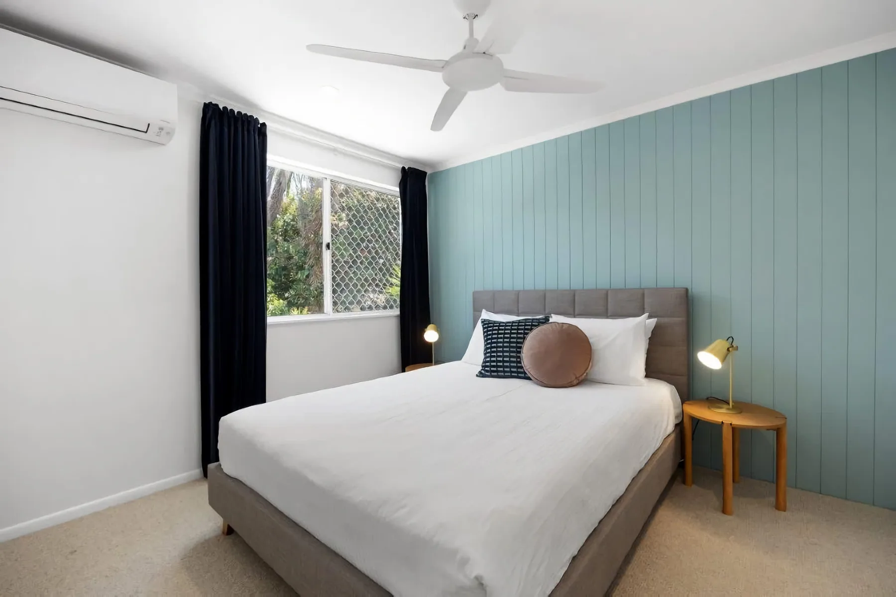 A bedroom with a bed beside a window and blue paneled wall.
