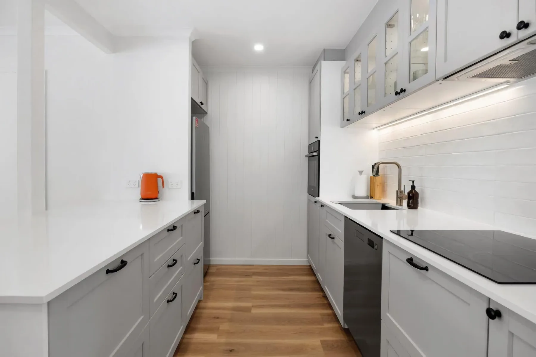 A bright modern kitchen with white cabinetry and wood flooring.