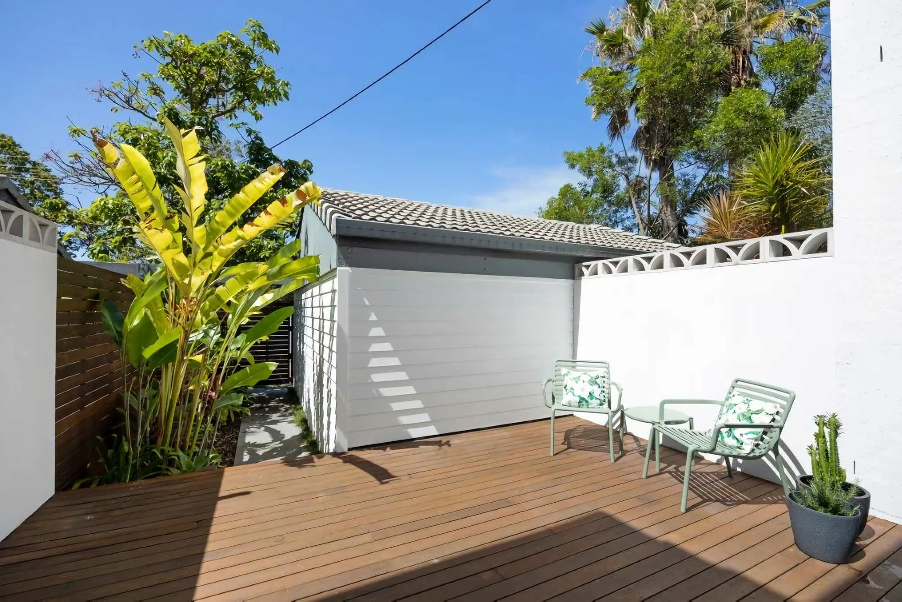 A sunlit outdoor deck with seating, plants, and a white garage door.