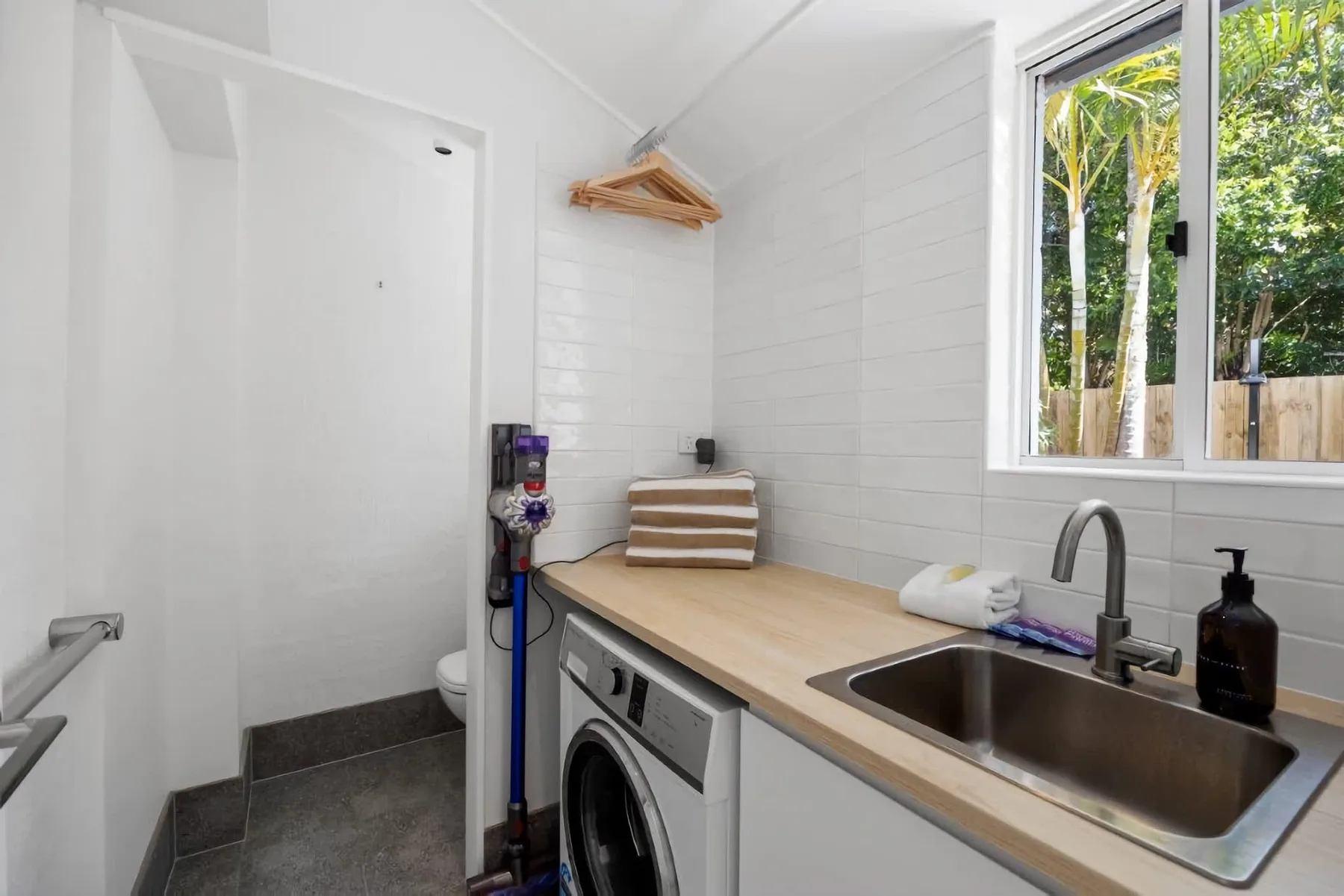 A bright laundry room with a washer, countertop, and sink beside a window.