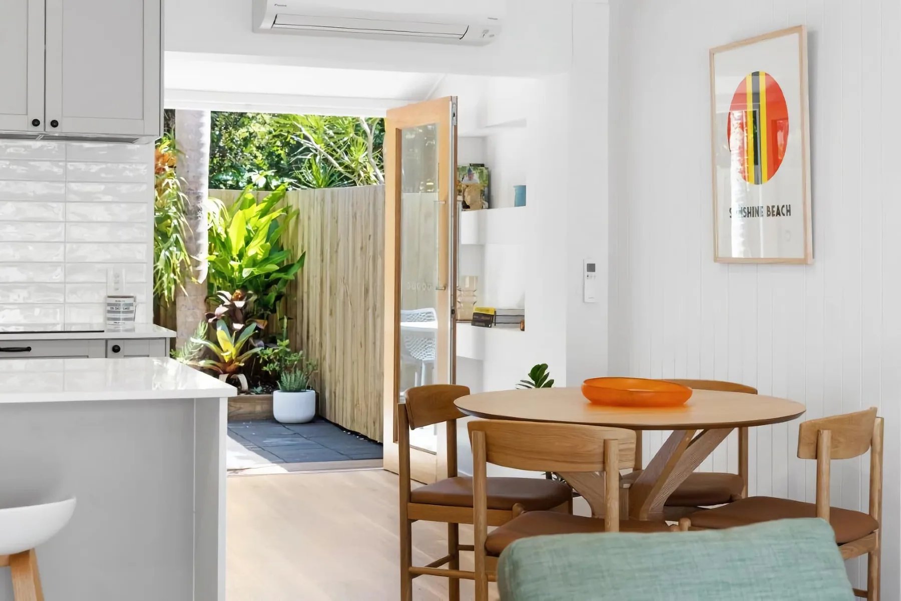 A bright dining area with a round wooden table beside an open door to a leafy patio.