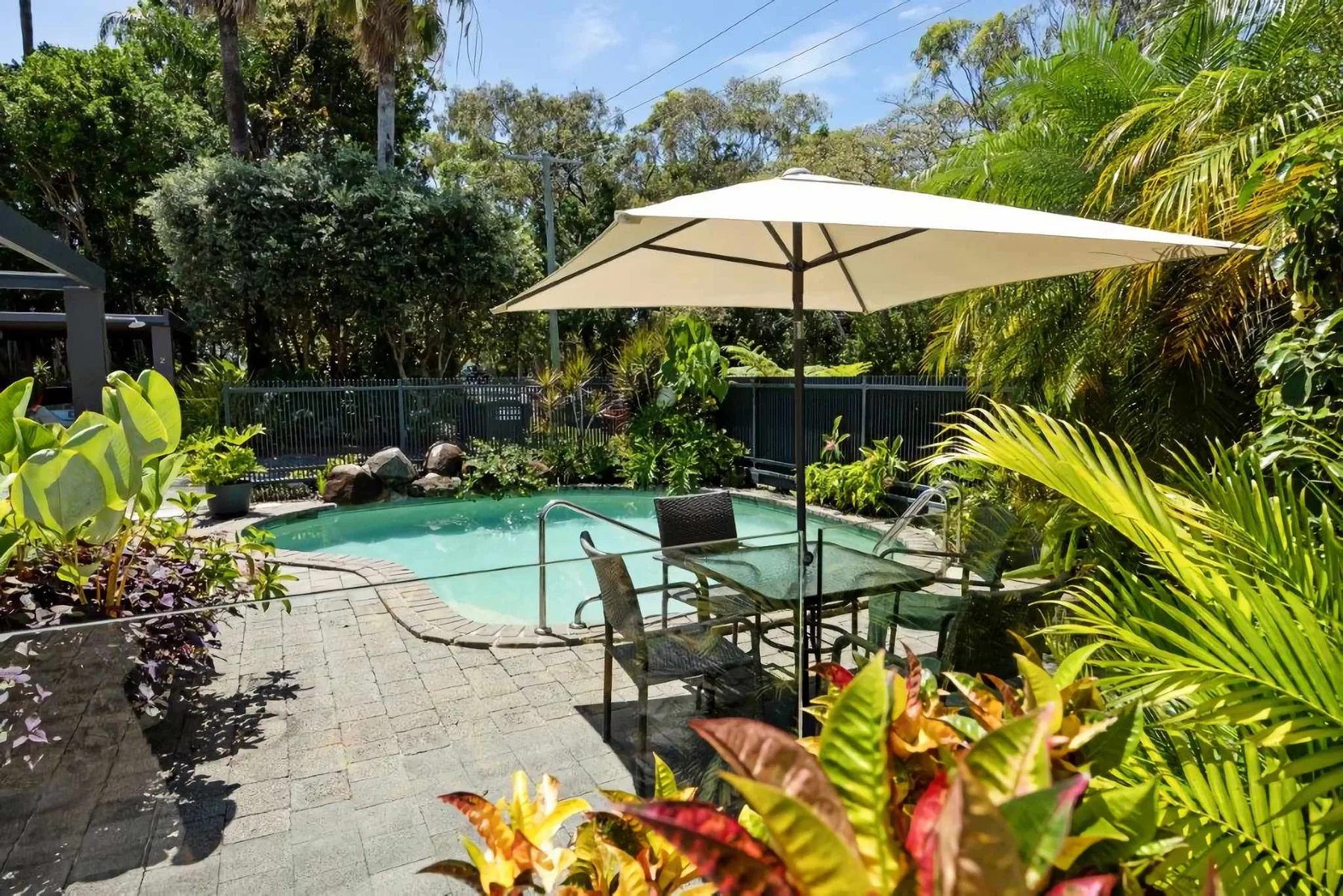 A garden pool is surrounded by tropical plants and a paved patio.