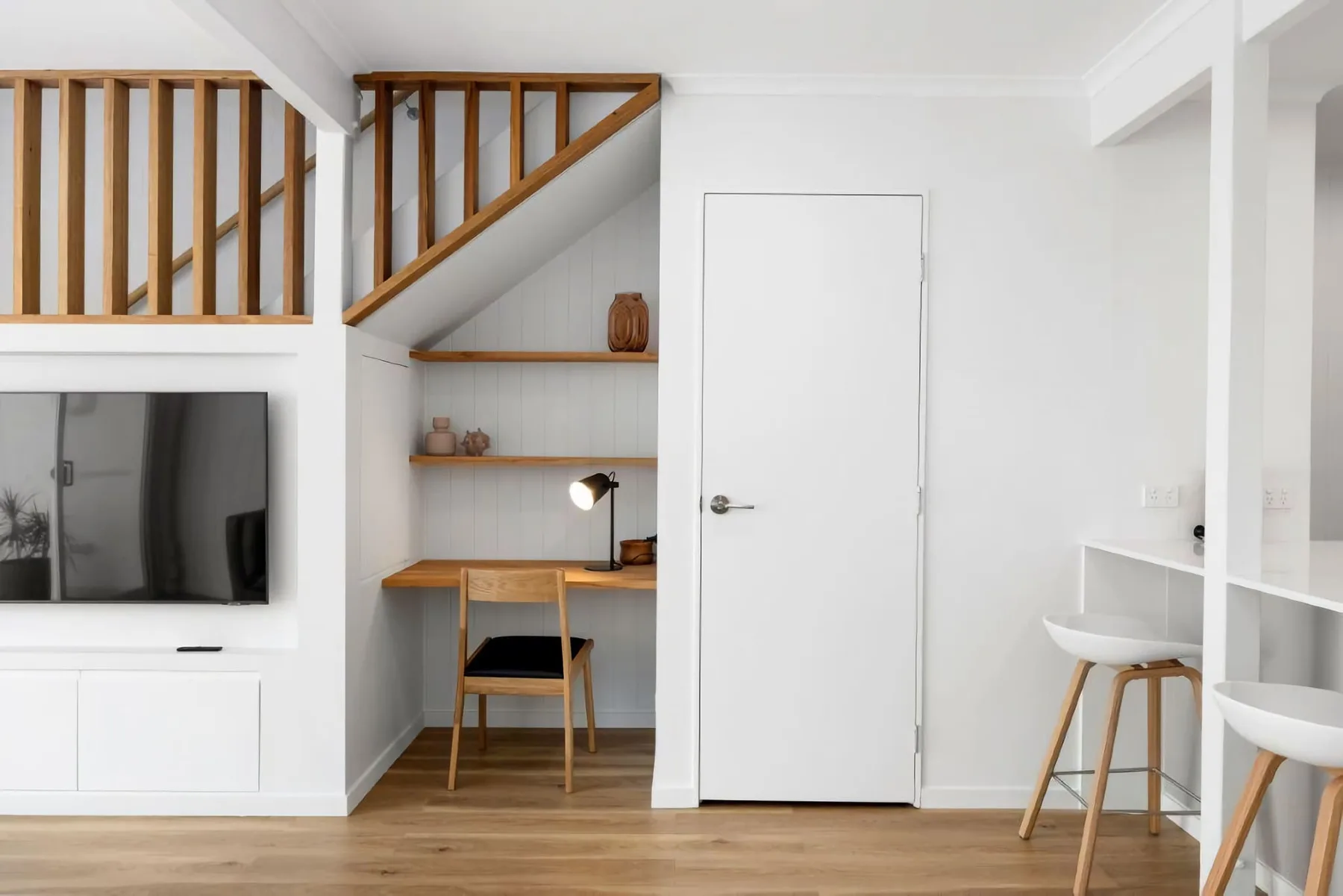 A bright interior with a wooden staircase, television, and compact desk area.