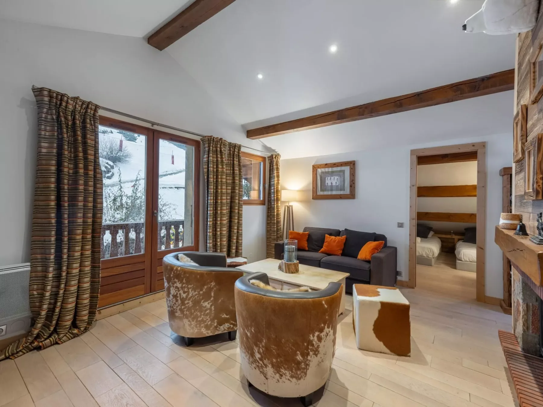 A living room with a sofa and two rounded armchairs beneath exposed wooden beams.