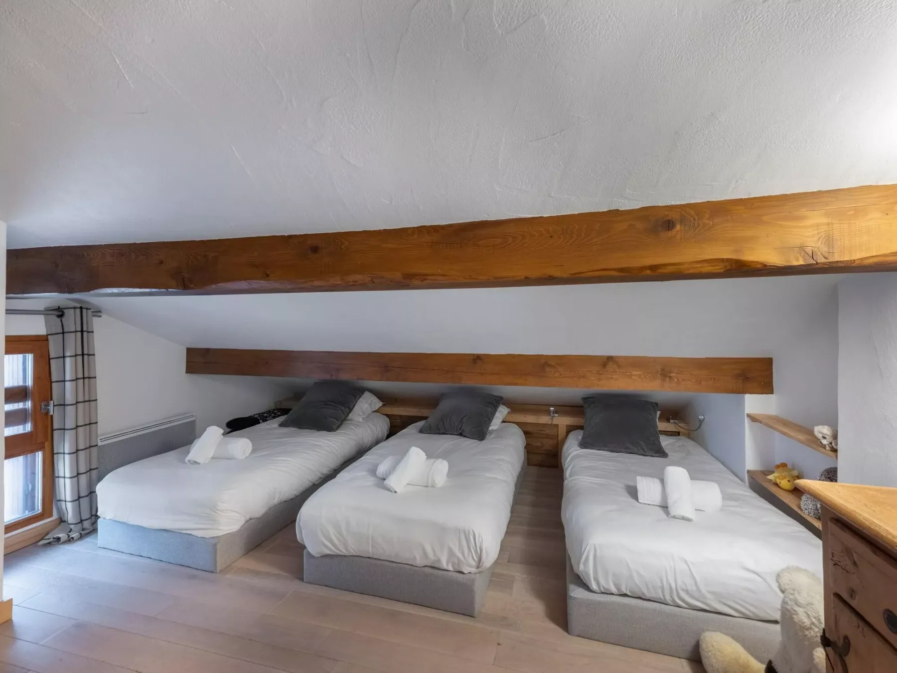 Un dormitorio con tres camas individuales bajo vigas de madera a la vista.