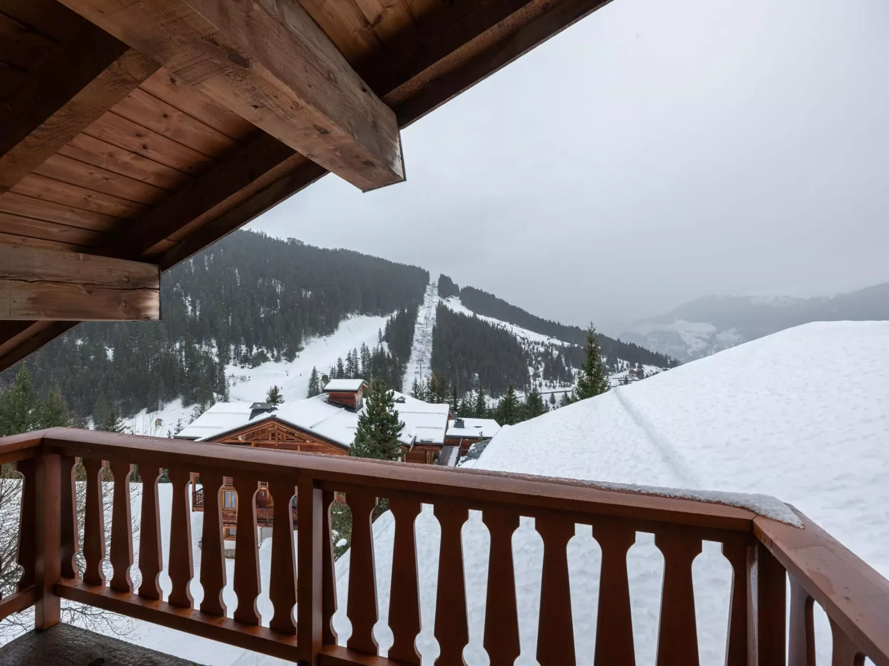 Un balcón de madera mira hacia laderas nevadas y una montaña boscosa.