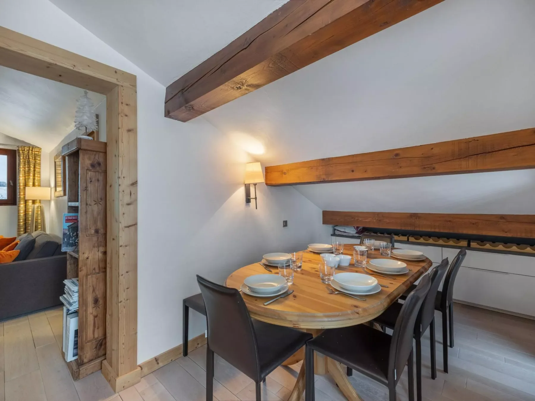 Comedor con una mesa redonda de madera y varias sillas bajo vigas de techo vistas.