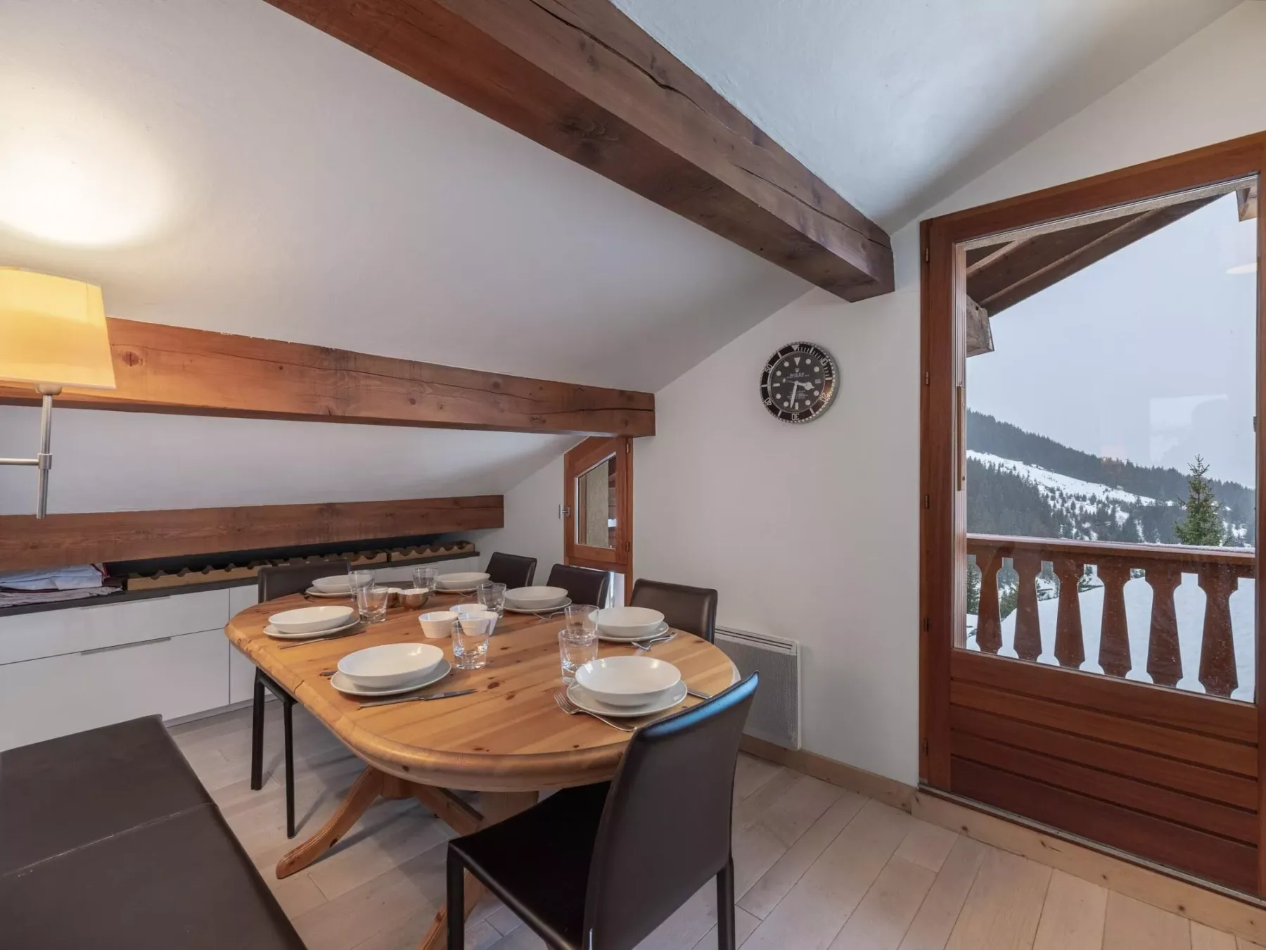 Comedor con una mesa de madera puesta con platos y vasos junto a una puerta al balcón.