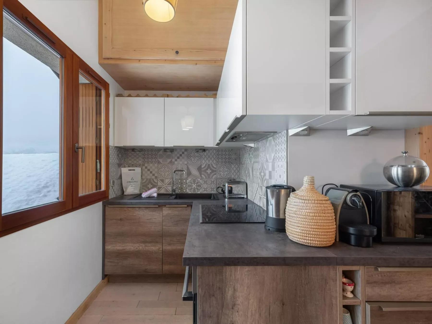 A compact kitchen with wood cabinetry, a dark countertop, and a window overlooking water.