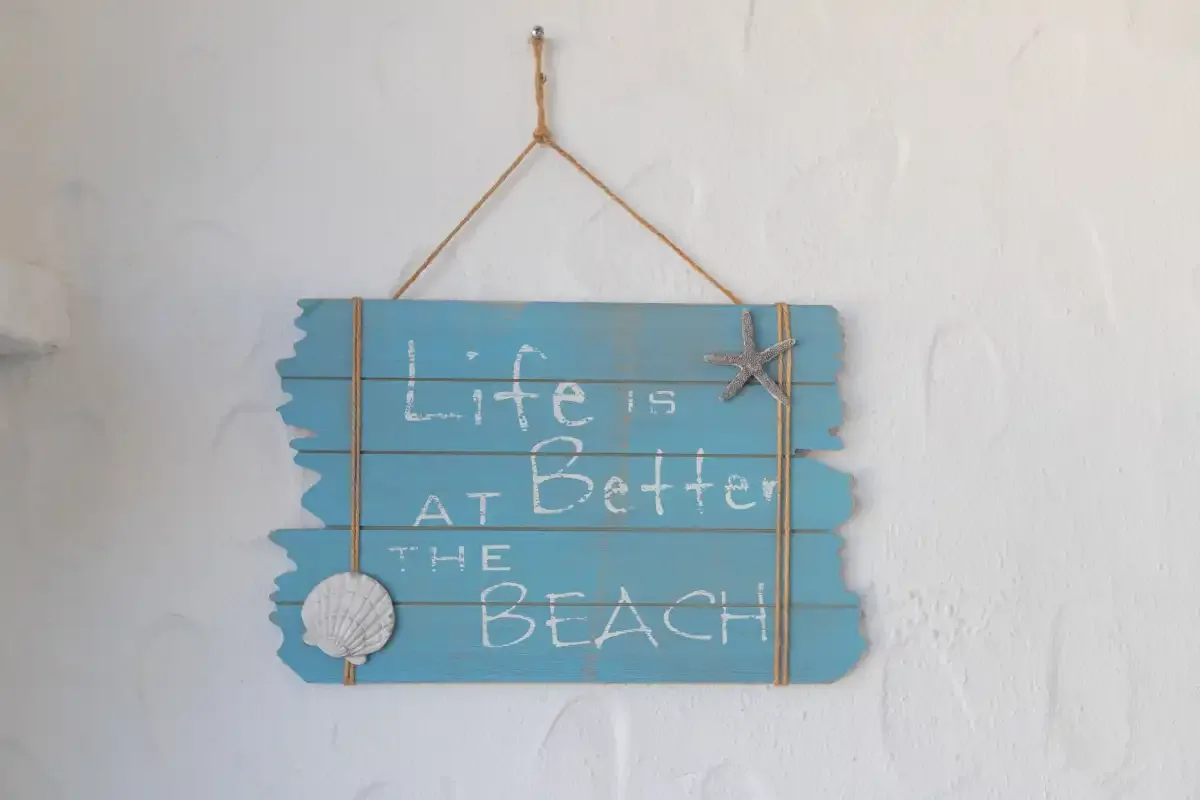 A blue beach-themed wall sign hangs against a white wall.