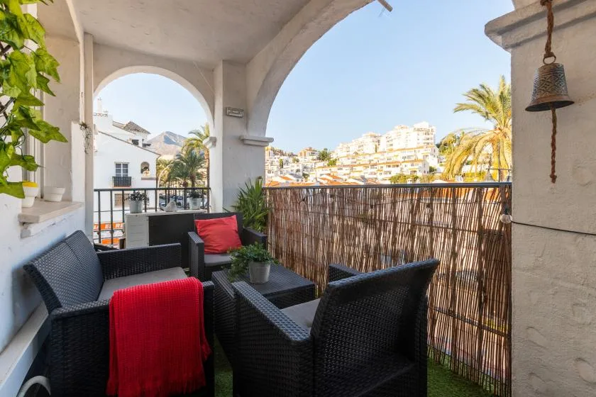 A covered balcony with dark outdoor seating and a view of nearby buildings.